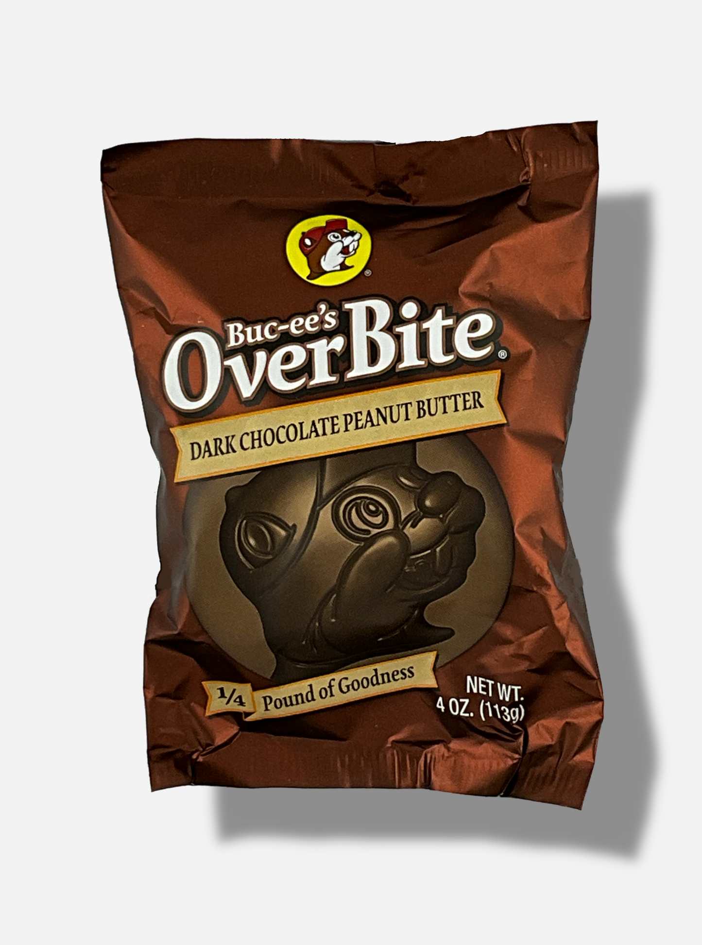 A picture of a package of a dark chocolate peanut butter Buc-ee's OverBite.  The package is metallic and dark brown, and features a large picture of the candy, which is shaped like the Buc-ee's beaver mascot logo.  The package reads BUC-EE's OVERBITE, then DARK CHOCOLATE PEANUT BUTTER, then 1/4 POUND OF GOODNESS.