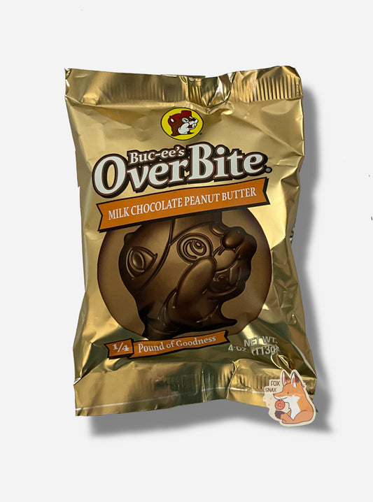 A picture of a package of a milk chocolate peanut butter Buc-ee's OverBite.  The package is metallic and light tan, and features a large picture of the candy, which is shaped like the Buc-ee's beaver mascot logo.  The package reads BUC-EE's OVERBITE, then MILK CHOCOLATE PEANUT BUTTER, then 1/4 POUND OF GOODNESS.