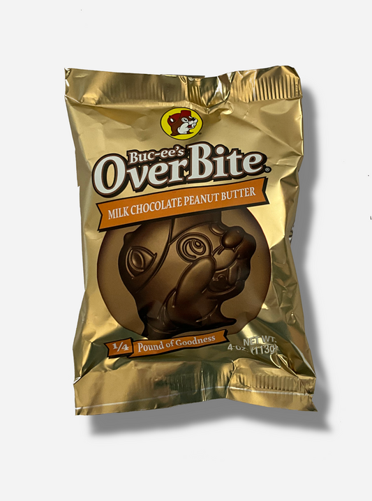 A picture of a package of a milk chocolate peanut butter Buc-ee's OverBite.  The package is metallic and light tan, and features a large picture of the candy, which is shaped like the Buc-ee's beaver mascot logo.  The package reads BUC-EE's OVERBITE, then MILK CHOCOLATE PEANUT BUTTER, then 1/4 POUND OF GOODNESS.