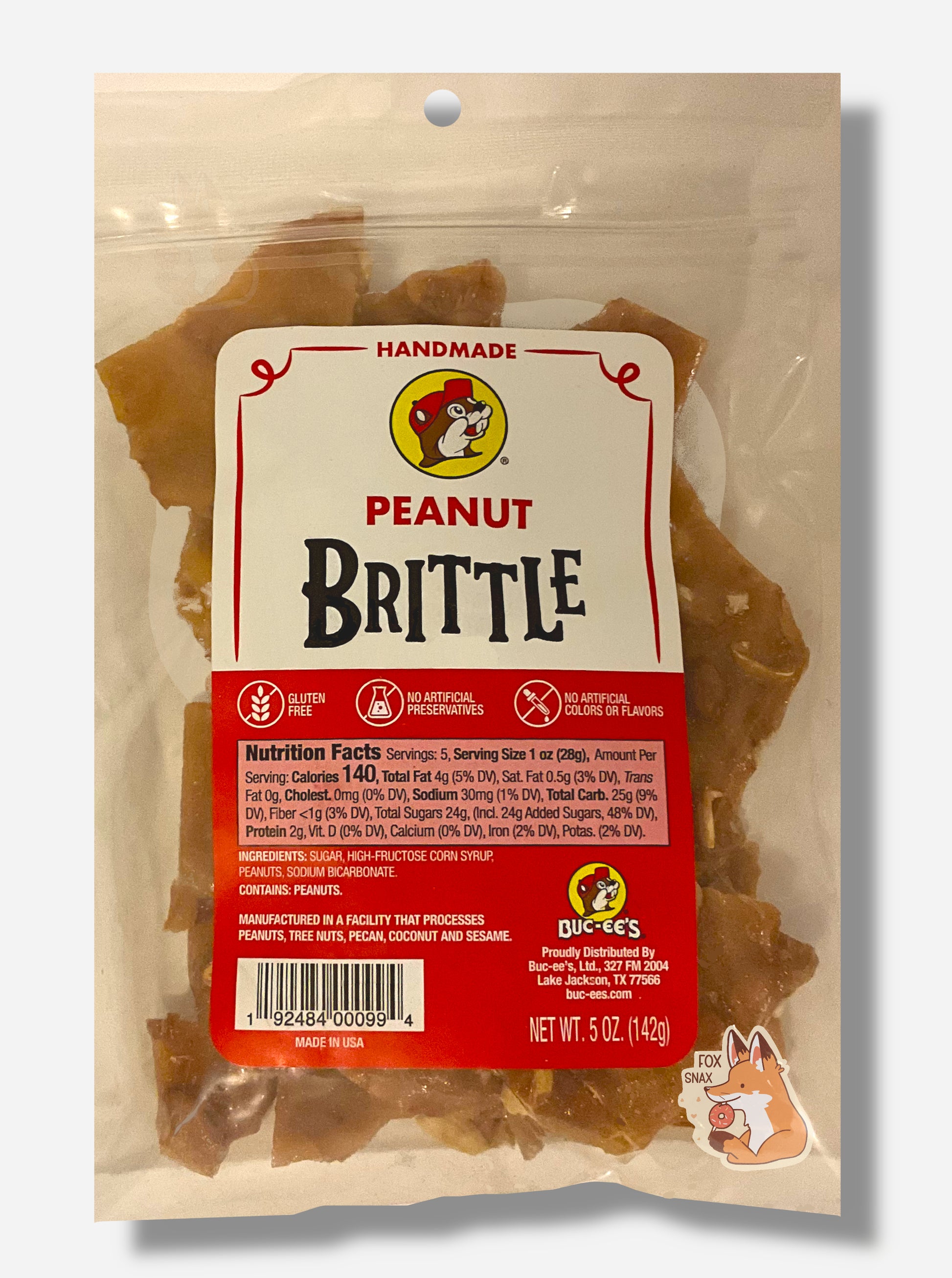 A picture of a small clear plastic bag of Buc-ee's Handmade Peanut Brittle.  The bag has a red and white rectangular sticker on it, and reads HANDMADE PEANUT BRITTLE, Gluten Free, No Artificial Preservatives, No Artificial Colors and Flavors.  Inside the plastic bag are brownish irregular shapes, the brittle, intermittently dotted with pieces of peanuts.