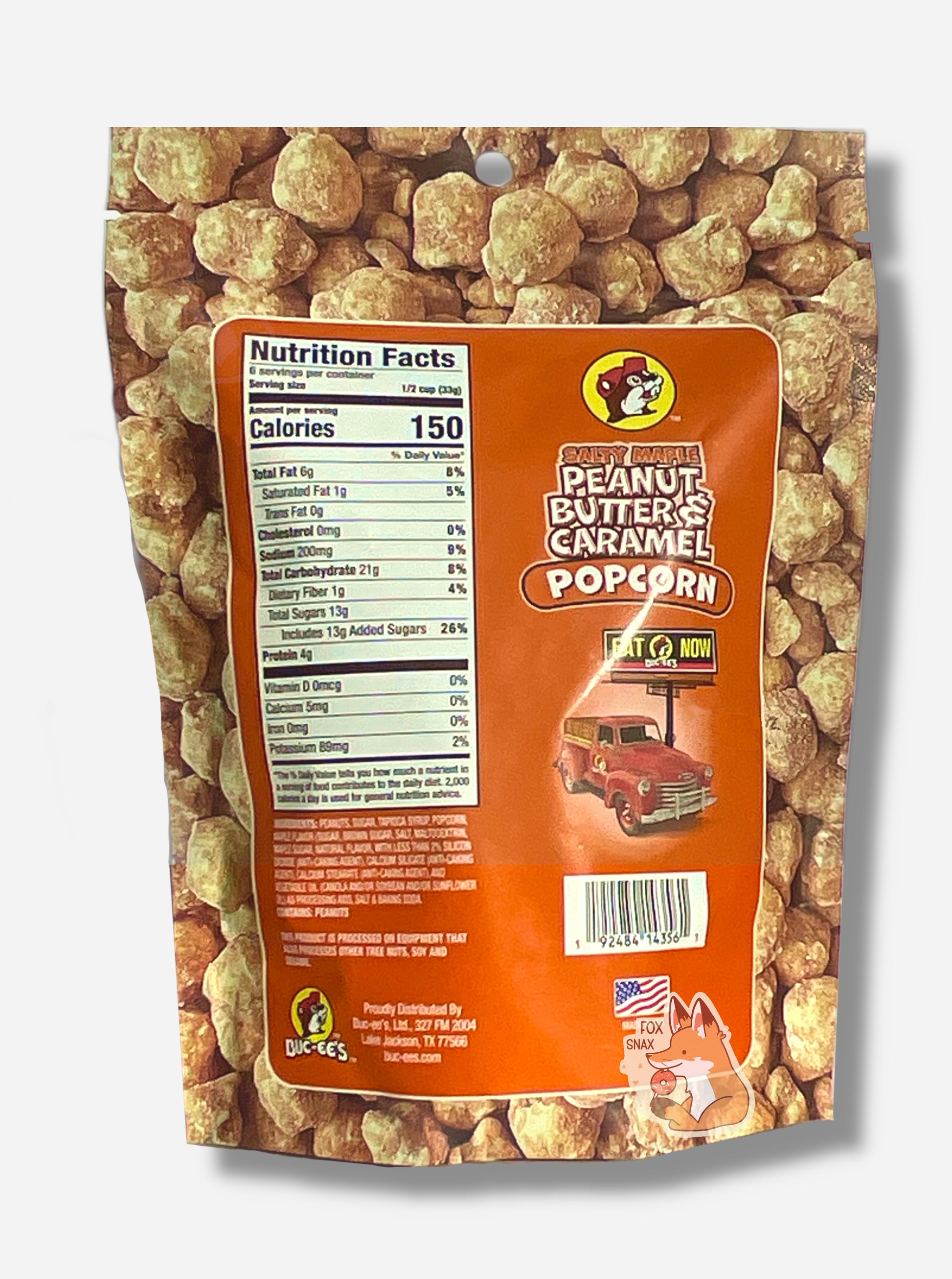A picture of the back of an orange  bag of Buc-ee's Salty Maple Peanut Butter & Caramel Popcorn.  The background is almost solely popcorn nuggets, each coated in brown salty maple peanut butter and caramel coating.  The right side reads SALTY MAPLE PEANUT BUTTER & CARAMEL POPCORN and has a picture of a red truck under a Buc-ee's EAT NOW sign.  Underneath that is the American flag, and says MADE IN USA.