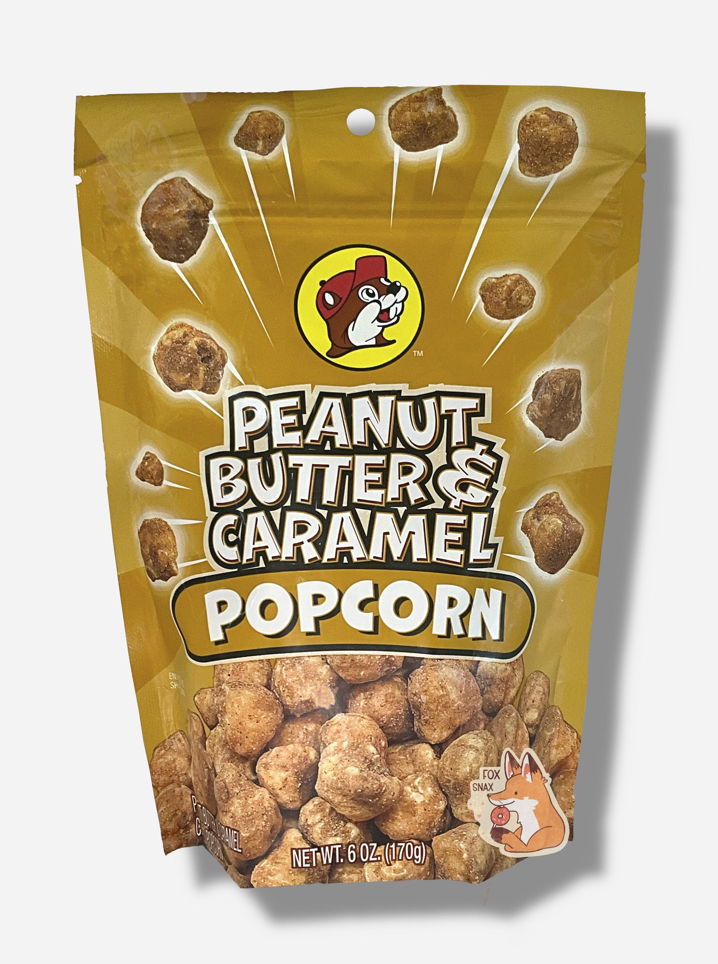 A picture of a tan/yellow bag of Buc-ee's Peanut Butter & Caramel Popcorn.  The front of the bag has a group of popcorn nuggets, each coated in brown peanut butter and caramel coating, exploding from the center.  A pile of popcorn is on the bottom.  The top center has the Buc-ee's logo, with cheerful beaver wearing a red ball cap, framed in a yellow circle, and reads PEANUT BUTTER & CARAMEL POPCORN.