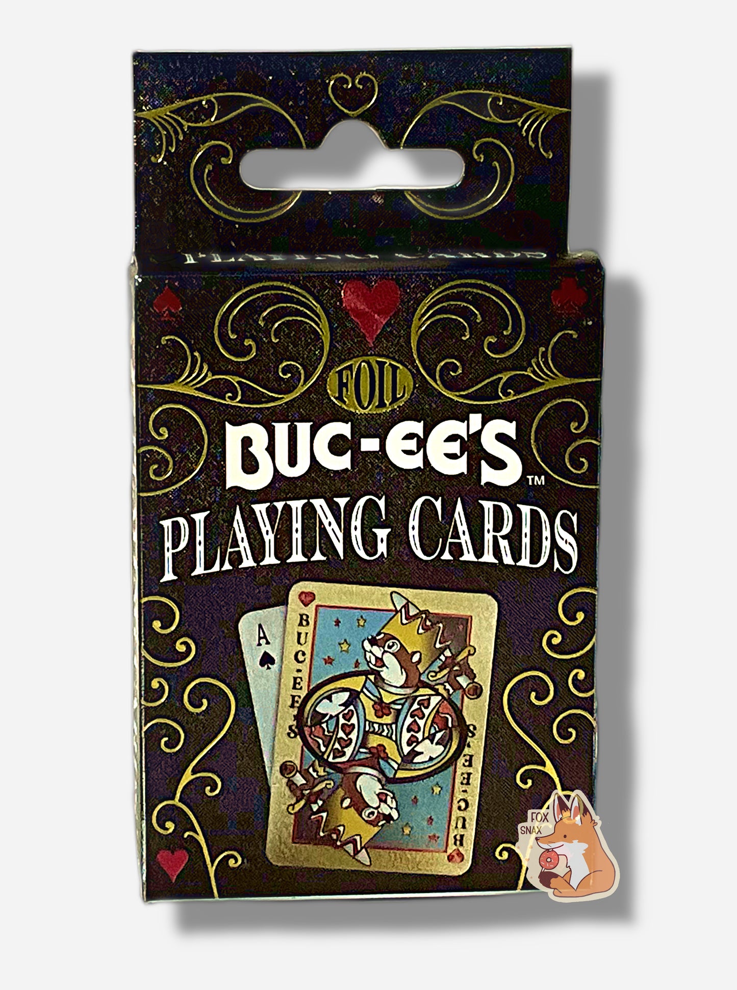 A picture of a pack of Buc-ee's Foil Playing Cards.  The pack is paper, black, with gold sparkles. The front of the pack has two cards at the top - the first the king of hearts, the second a "normal" ace of spades. The background is black with ornate gold swirls and red hearts, clubs, and spades.  In the middle reads FOIL in gold foil, then BUC-EE'S PLAYING CARDS.