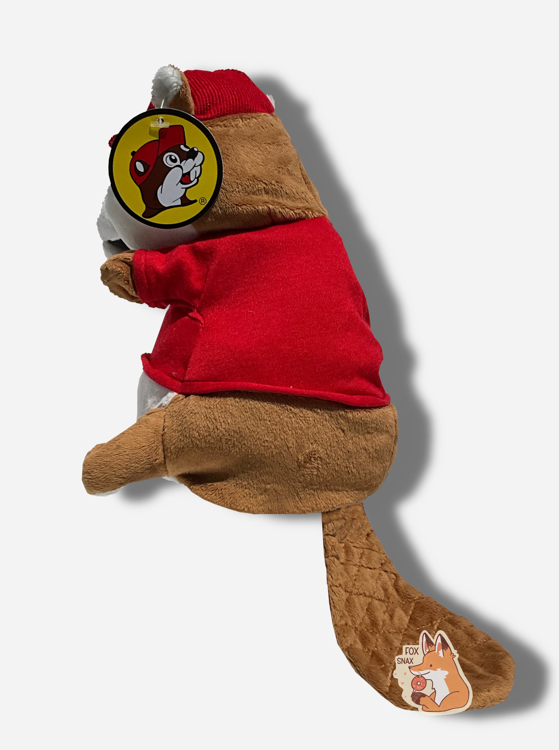 The side of a Buc-ee the Beaver hand puppet.  Buc-ee is covered in brown and white fur, and has a big buck-tooth grin.  On his head is a red ball cap, and he's wearing a red t-shirt with the Buc-ee's logo.  Buc-ee's has a large brown beaver tail poking from his backside.
