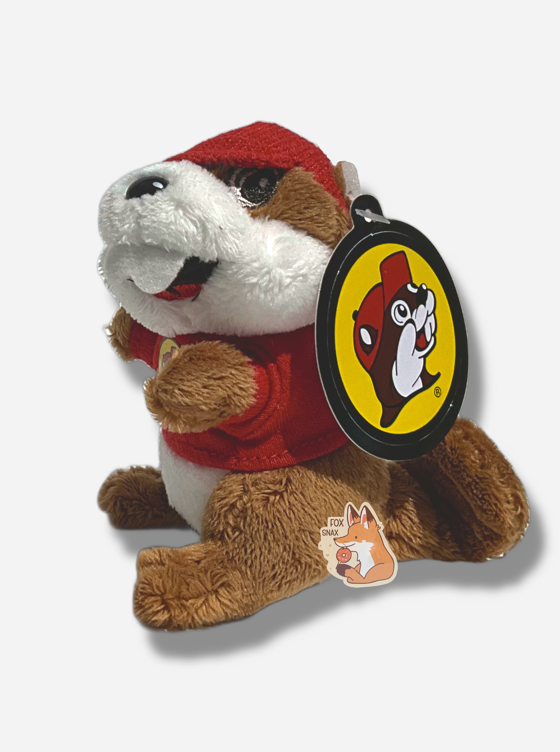 A picture of the side of a small fuzzy Buc-ee the Beaver keychain.  The keychain is made of fuzzy fur-like material, and is of Buc-ee the Beaver:  a brown-furred beaver with a serious overbite and fat beaver tail, wearing a red Buc-ee's t-shirt and a red ball cap.  The back of the hat has a small metal clasp to hook the keychain to the rest of one's keys.