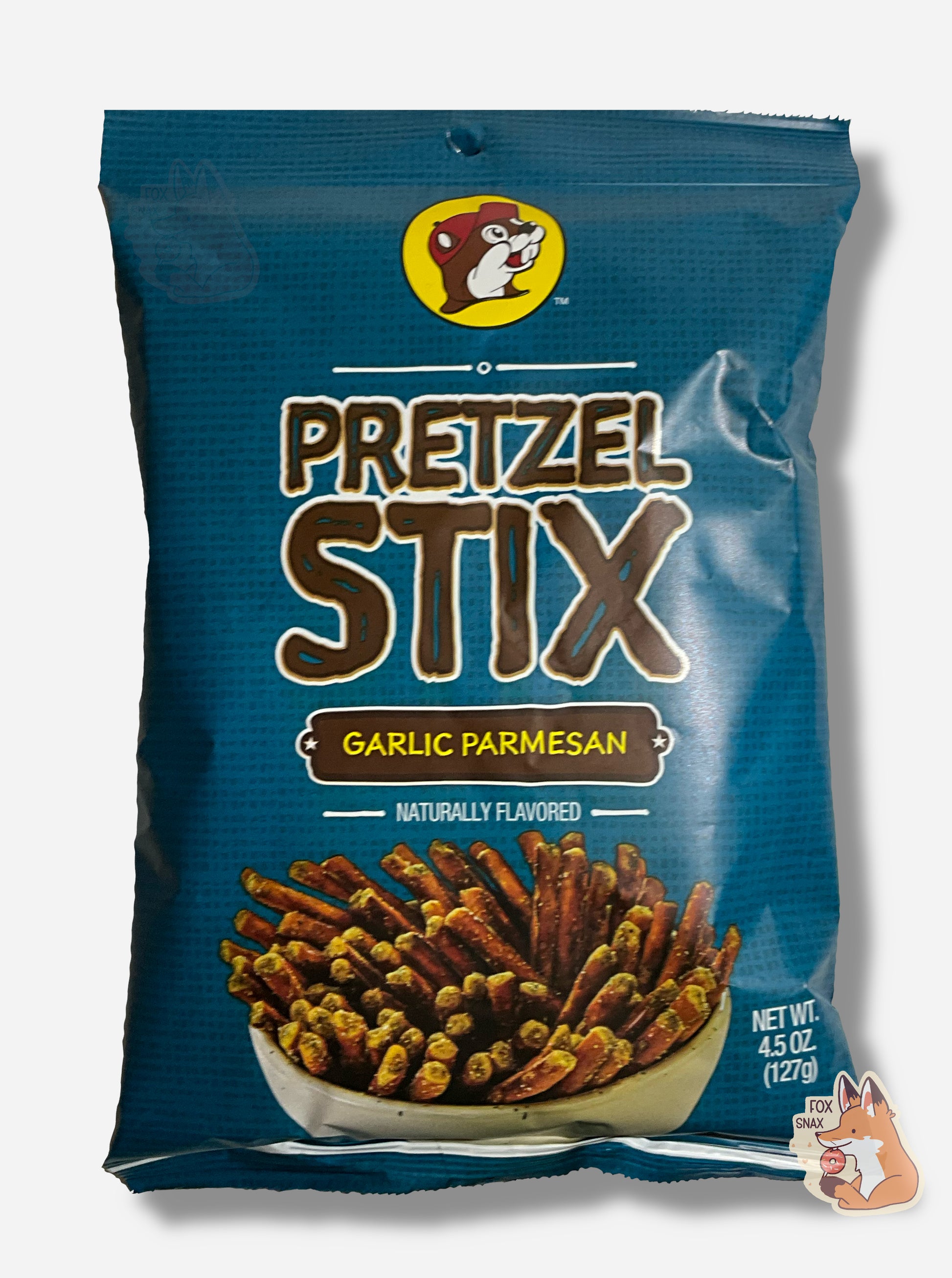 A picture of the front of a blue bag of Buc-ee's Pretzel Stix, Garlic Parmesan flavor.  The bag reads NATURALLY FLAVORED.  At the top is the Buc-ee's logo - a cheerful beaver wearing a red ball cap.  The middle reads PRETZEL STIX in a brown font, then GARLIC PARMESAN, then NATURALLY FLAVORED.  A large white bowl containg a plethora of coated pretzel sticks is on the bottom.