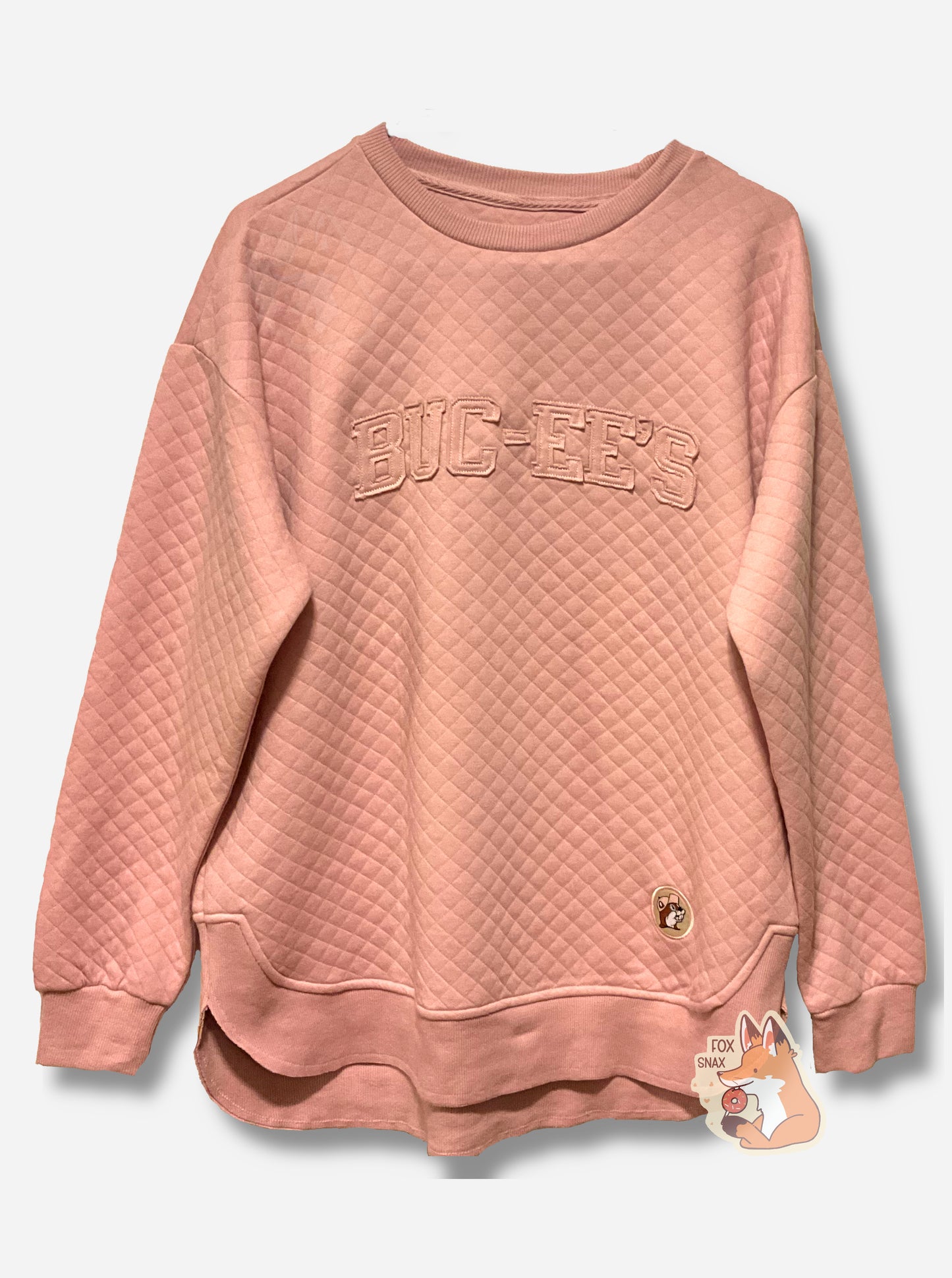 A picture of a light pink, quilted pattern fleece sweater/sweatshirt.  The left side, near the bottom of the shirt, shows a Buc-ee's logo, with Buc-ee wearing a pink hat.  Across the chest reads the word BUC-EE'S.