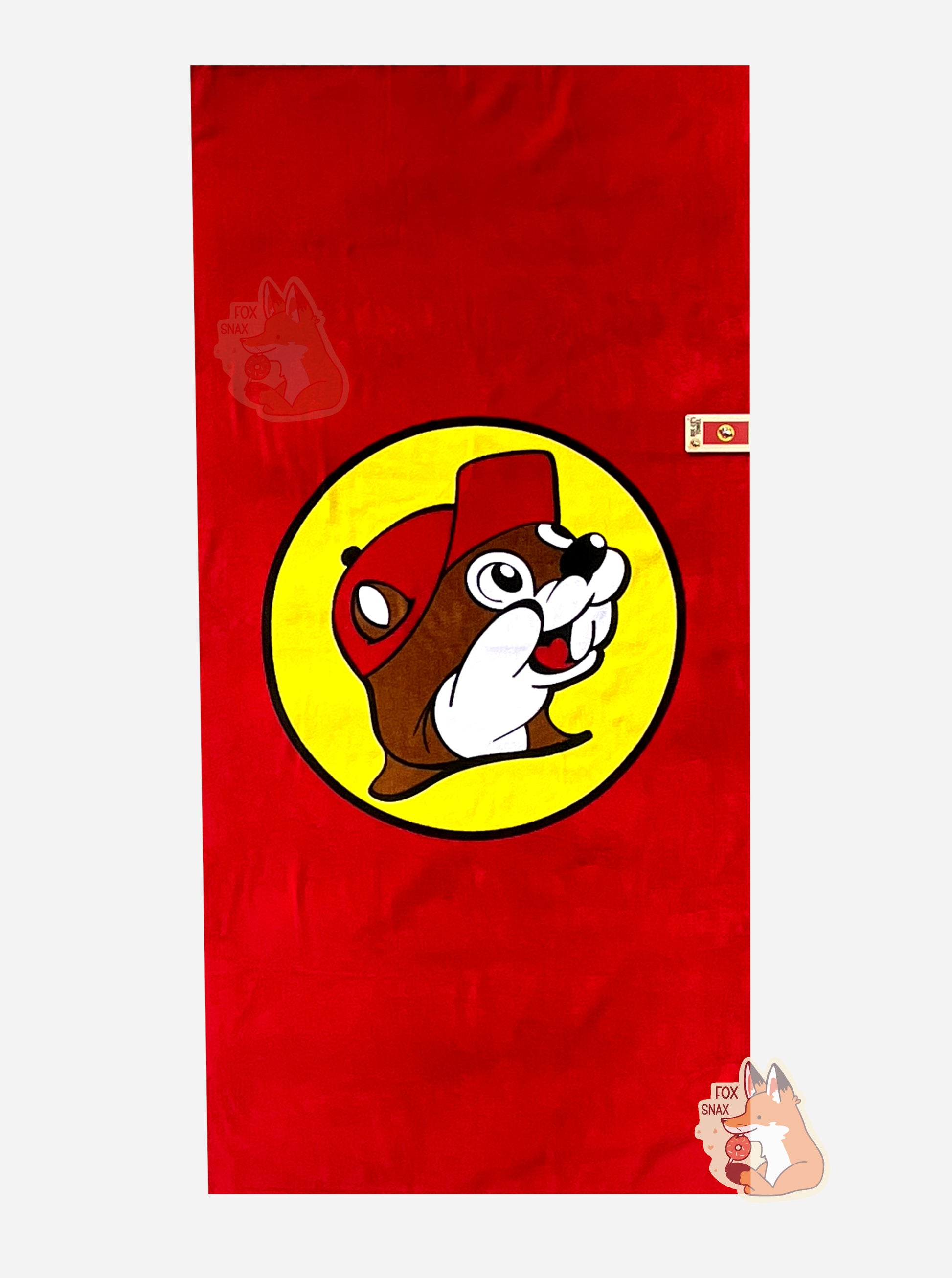 A picture of an unwrapped, 32x64, fluffy beach towel, adorned with a single Buc-ee The Beaver logo.   Buc-ee is framed by a yellow circle, and is wearing a red ball cap. A small paper tag on the bottom states: BUC-EE'S TOWEL. 32 in x 64 in. 100% Cotton.