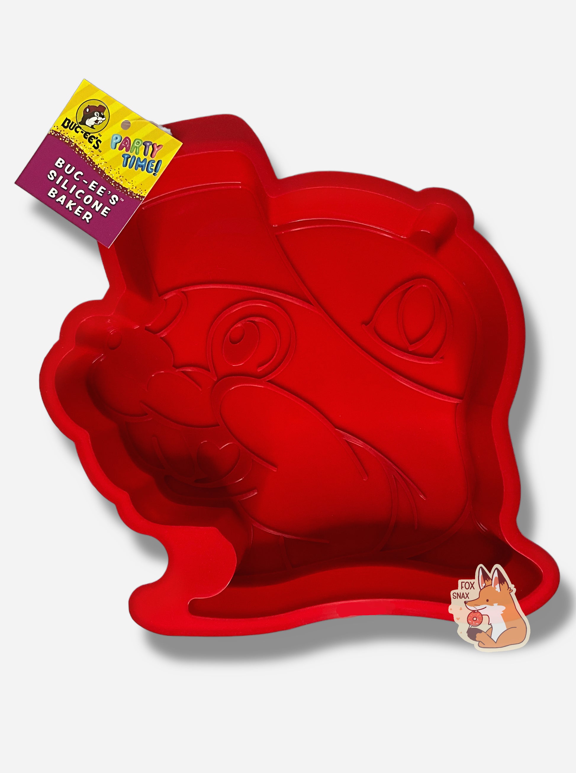 A picture of a bright red, floppy, silicone baking tray.  The tray is shaped like Buc-ee The Beaver's Head, and has the icon with a cheerful grin, ballcap, and buck teeth.  The tag attached to the tray reads PARTY TIME!  BUC-EE's SILICONE BAKER