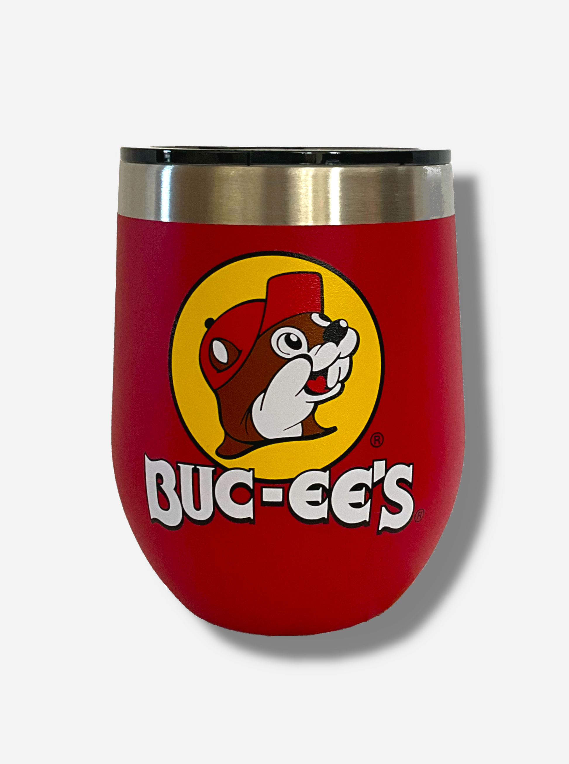 A picture of a short, red, sorta squatty tumbler, with a big picture of Buc-ee The Beaver on it.  Underneath the picture is the BUC-EE'S logo. The surface is smooth and red, as it is red paint covering stainless steel.  The top of the tumbler and a slider on top to open and close it are plastic.  The top of the tumbler is lined with a stainless steel band.  