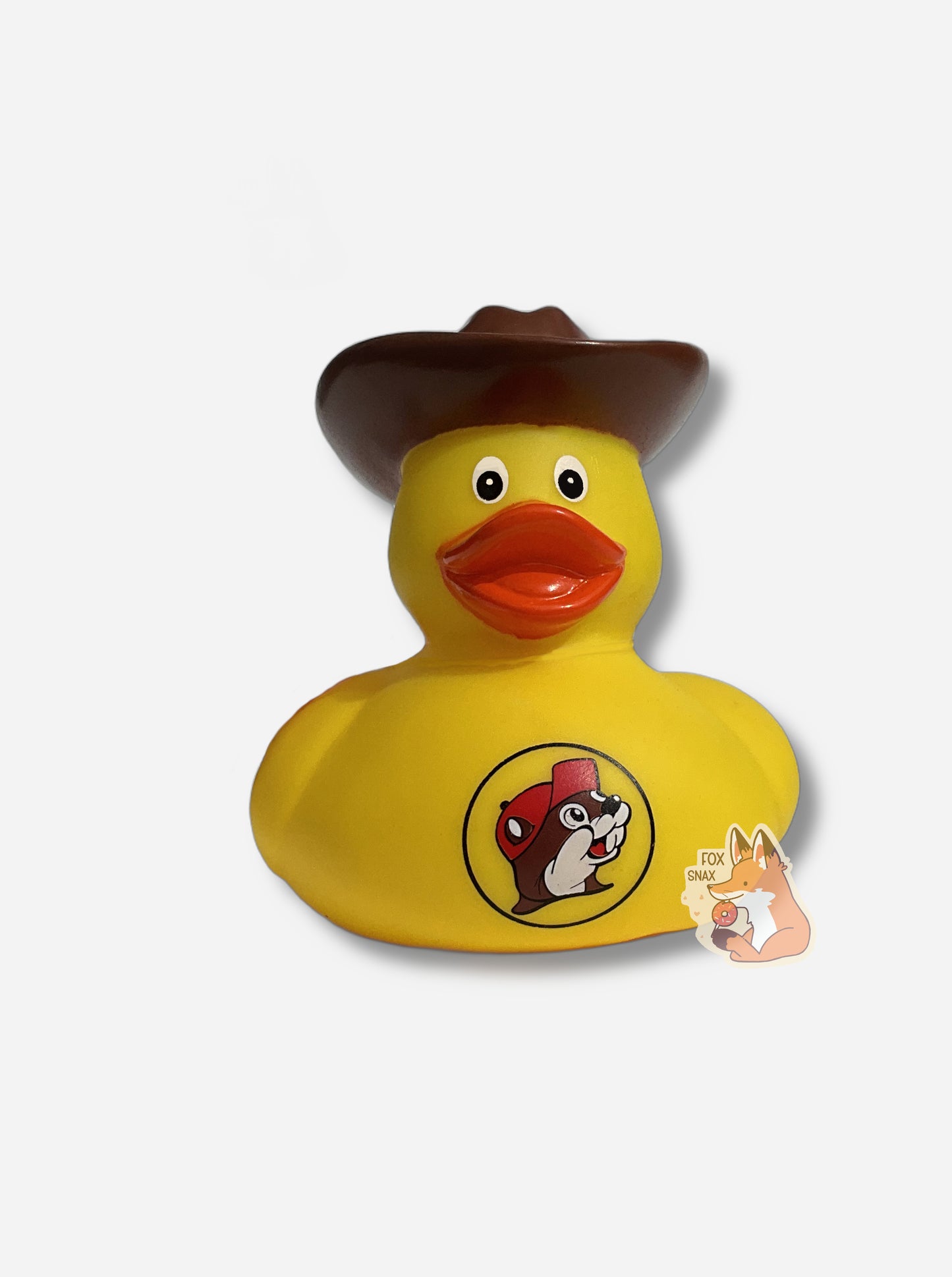 A picture of the front of a yellow rubber duck wearing a large brown cowboy hat. The duck has an orange beak, and is made of plastic.  It is wearing a dark brown hat on its head, and a red t-shirt around its body.  The front of the t-shirt has the Buc-ee's logo: a cheerful, brown furred beaver with a significant overbite, which is wearing a red ball cap.