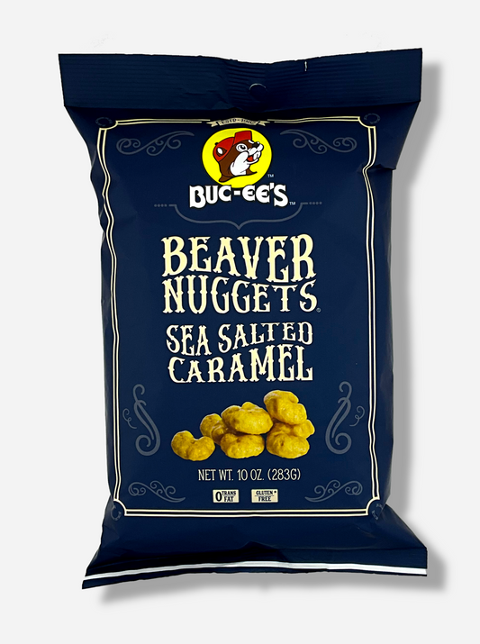 A picture of the front of a opaque, dark blue bag of Buc-ee's Beaver Nuggets, Sea Salted Caramel, which are puffed corn snack with caramel flavors.  It has a picture of Buc-ee the Beaver on the top. The bag reads: 0 Trans Fat.  Gluten Free.