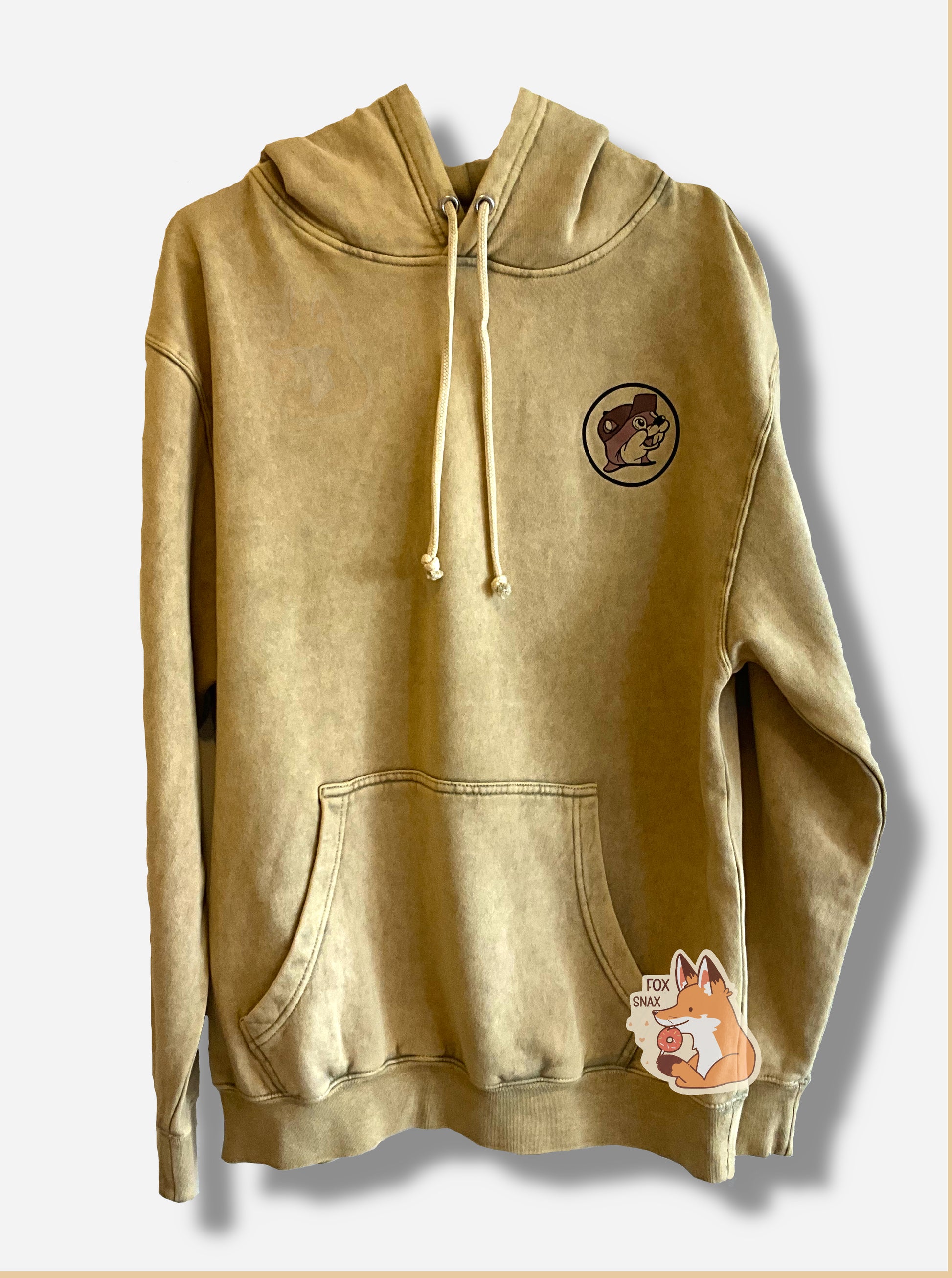 A picture of a large, tan hoodie sweatshirt.  On the left side is the Buc-ee's logo, all in tan.  The front of the hoodie features a center pocket for the hands.  A string can be seen poking out of two metal eyeholes on the front.