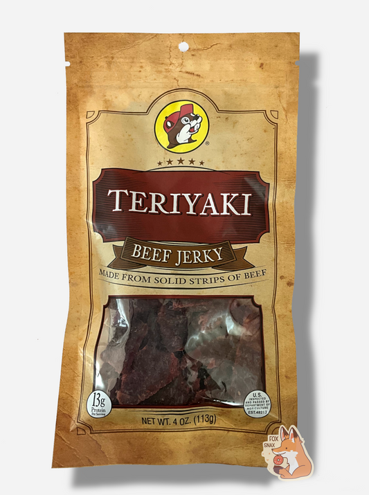A picture of the front of a tan plastic bag of Buc-ee's Teriyaki Garlic Beef Jerky.  The logo is in red-brown with white text.The label underneath reads 'Made From Solid Strips Of Beef'.A small window on the bottom of the bag shows the dark brown/red dried jerky inside.  The bag has a picture of Buc-ee the Beaver on it.