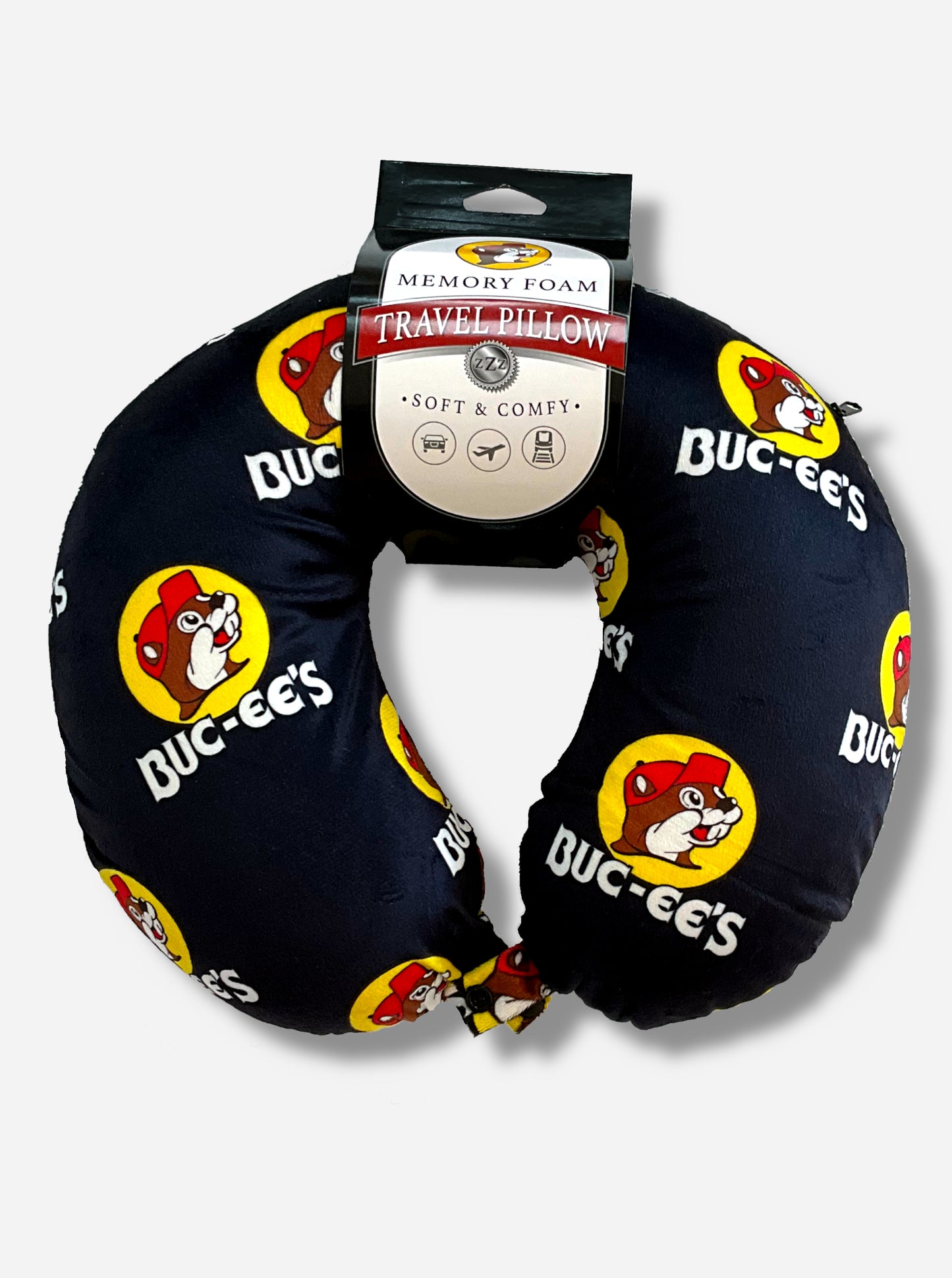 A picture of a u-shaped, memory foam travel pillow.  It is adorned with the Buc-ee The Beaver logo, and says BUC-EE'S underneath each logo.  The rest of the neck pillow is black.  The label on the pillow reads MEMORY FOAM TRAVEL PILLOW.  SOFT AND COMFY.  Underneath that, there are icons of a car, plane, and train.  A zipper can be seen on the right side of the pillow.